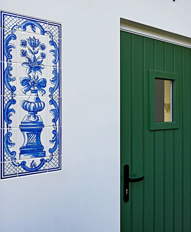 Glad gepleisterde witte gevel met een tegeltableau en een groene voordeur