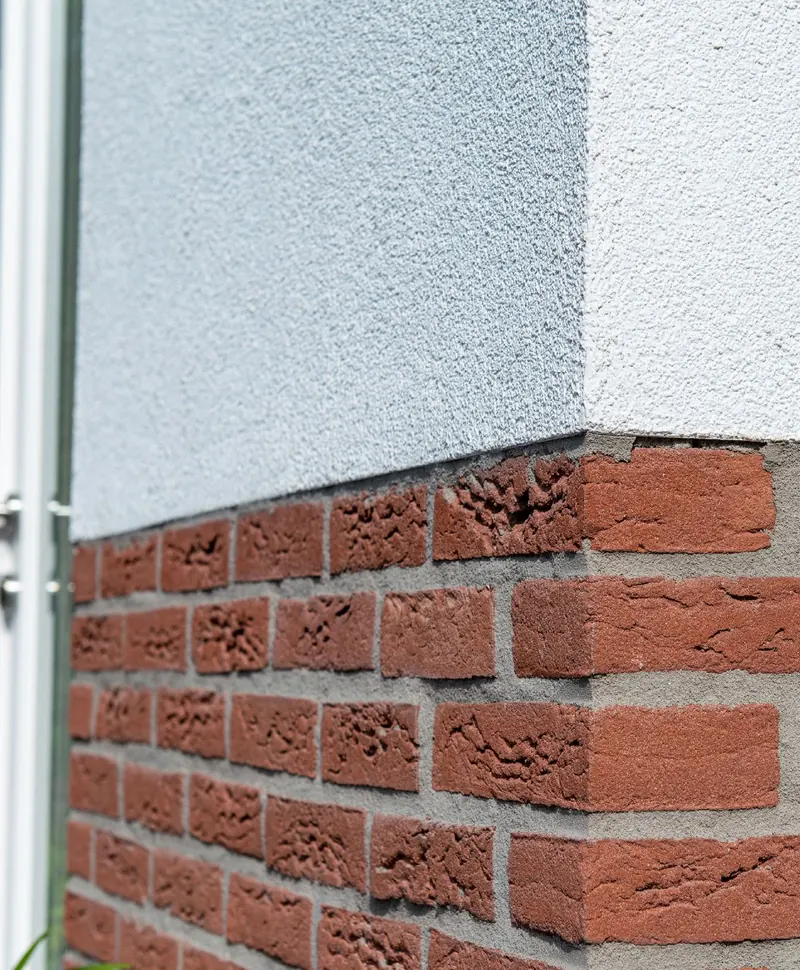 Hoek waar strak wit stucwerk overgaat in rode steenstrips