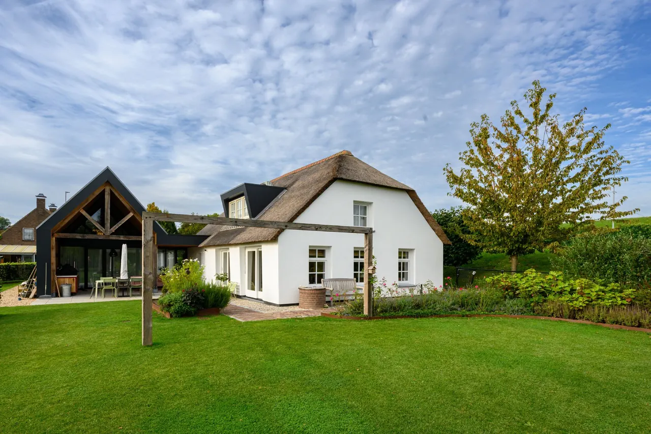 Woonboerderij met rieten kap en witte gevels onder een wolkenlucht