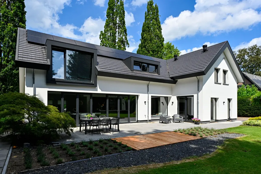 Opgeleverde witte woning met donkere dakkapellen en een tuin met terras