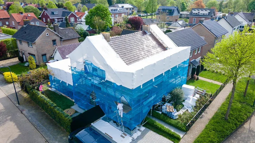 Luchtfoto van een woning in Empel, volledig in de steiger met afgesloten netten